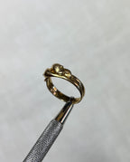 gold ring with two snake heads, held by silver tool above soft cream background 