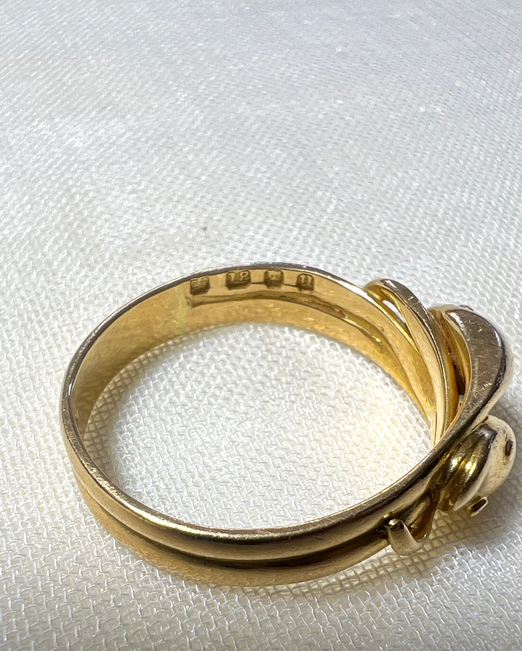 close up of gold ring with visible hallmark, makings 18, lions head and letter U. resting on white fabric background