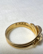 close up of gold ring with visible hallmark, makings 18, lions head and letter U. resting on white fabric background