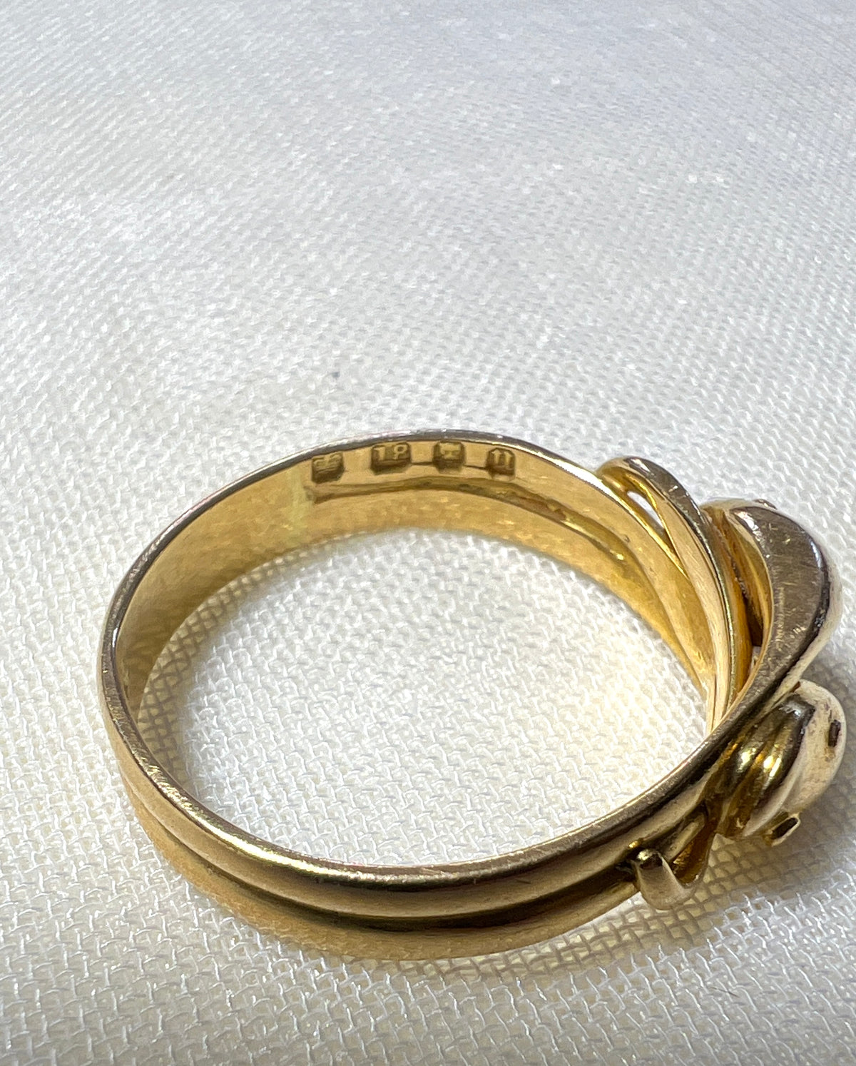 close up of gold ring with visible hallmark, makings 18, lions head and letter U. resting on white fabric background