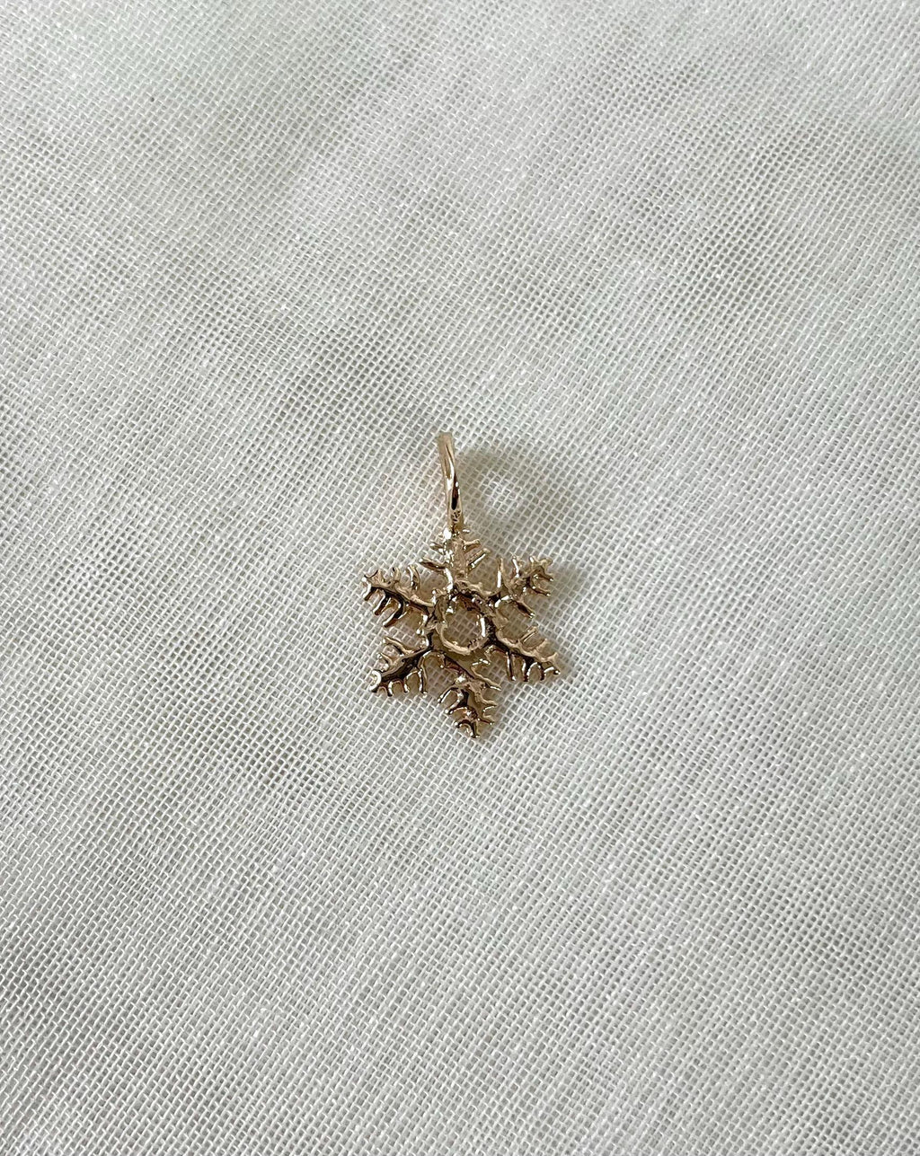 Gold snowflake-shaped pendant on a white fabric background