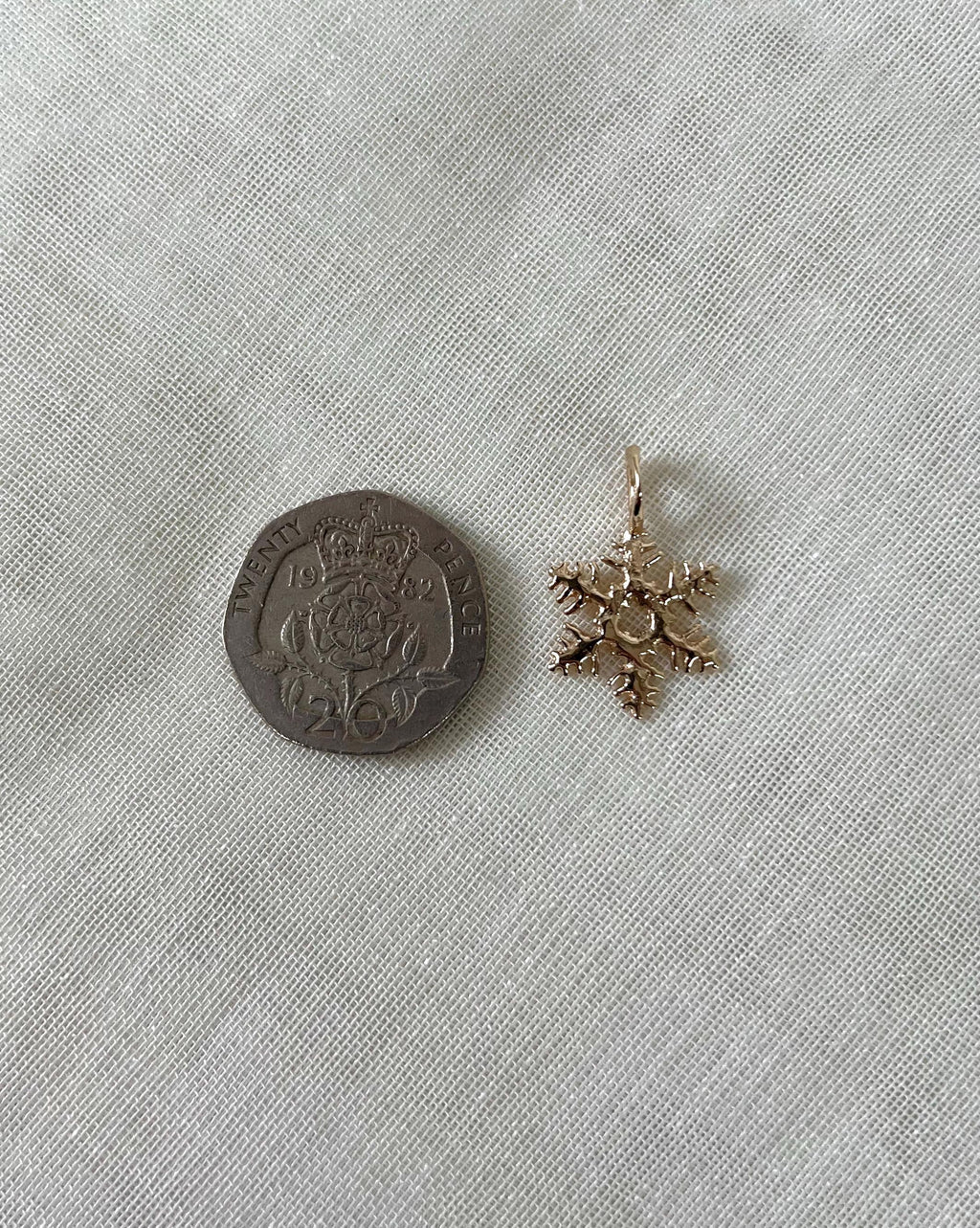 gold snowflake charm next to 20 pence coin on white fabric background 