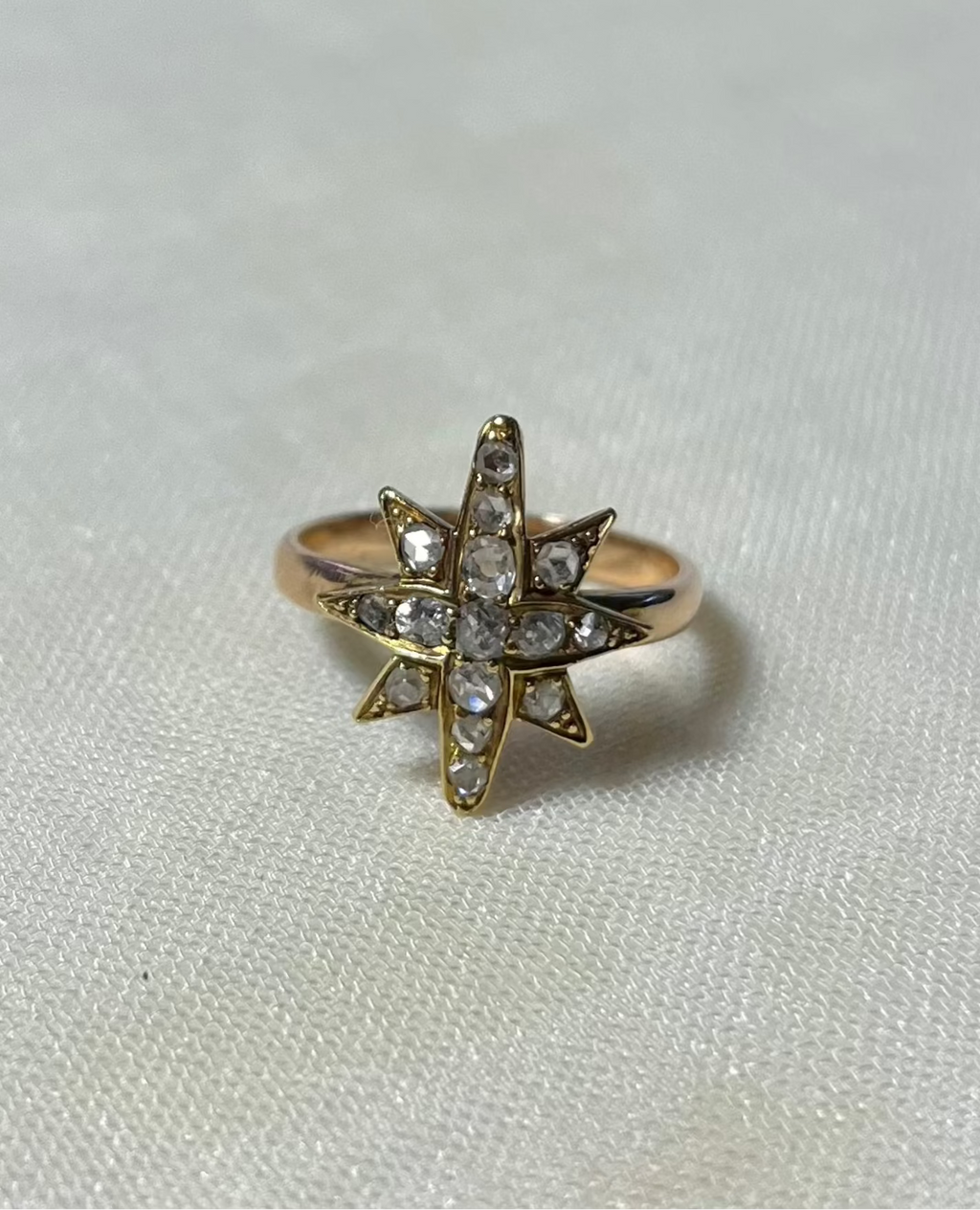 a gold star ring set with diamonds, resting on white fabric background