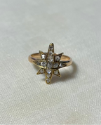 a gold star ring set with diamonds, resting on white fabric background
