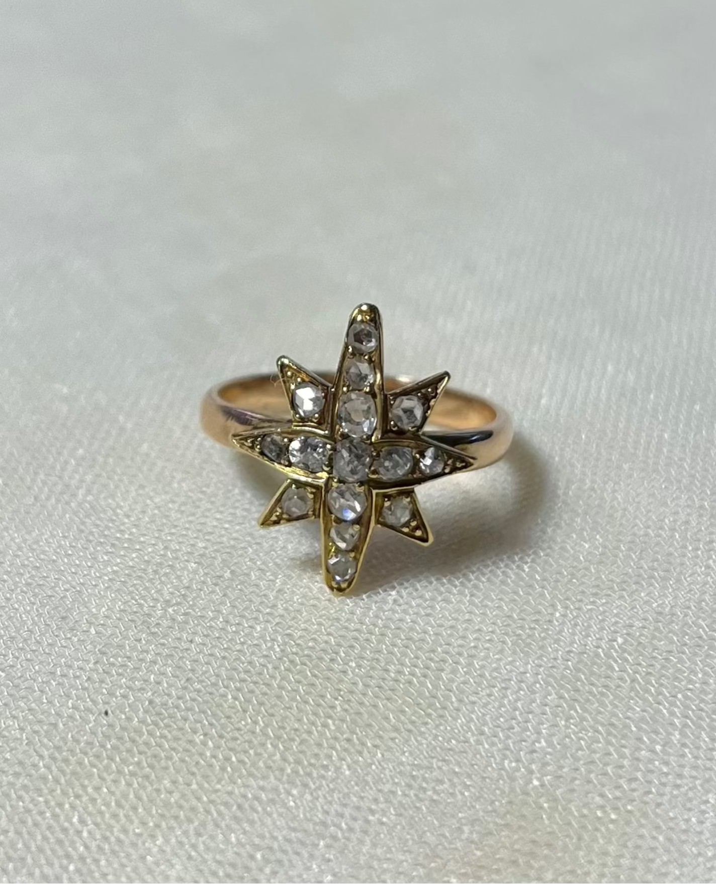 a gold star ring set with diamonds, resting on white fabric background