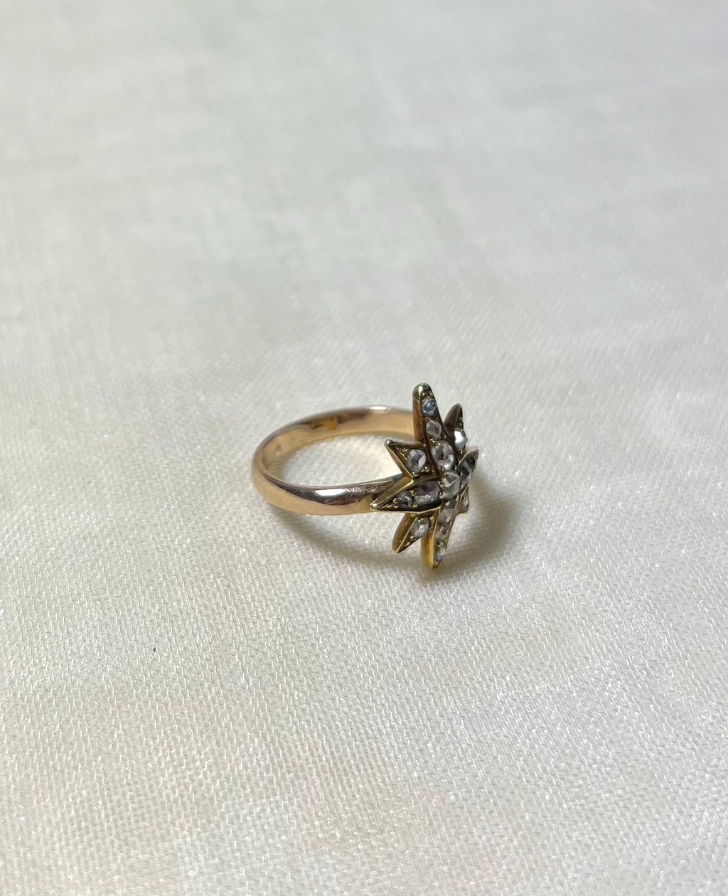 gold star ring set with diamonds on white fabric background 