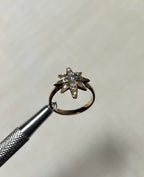 a gold star ring set with diamonds, held by silver tool above white background 