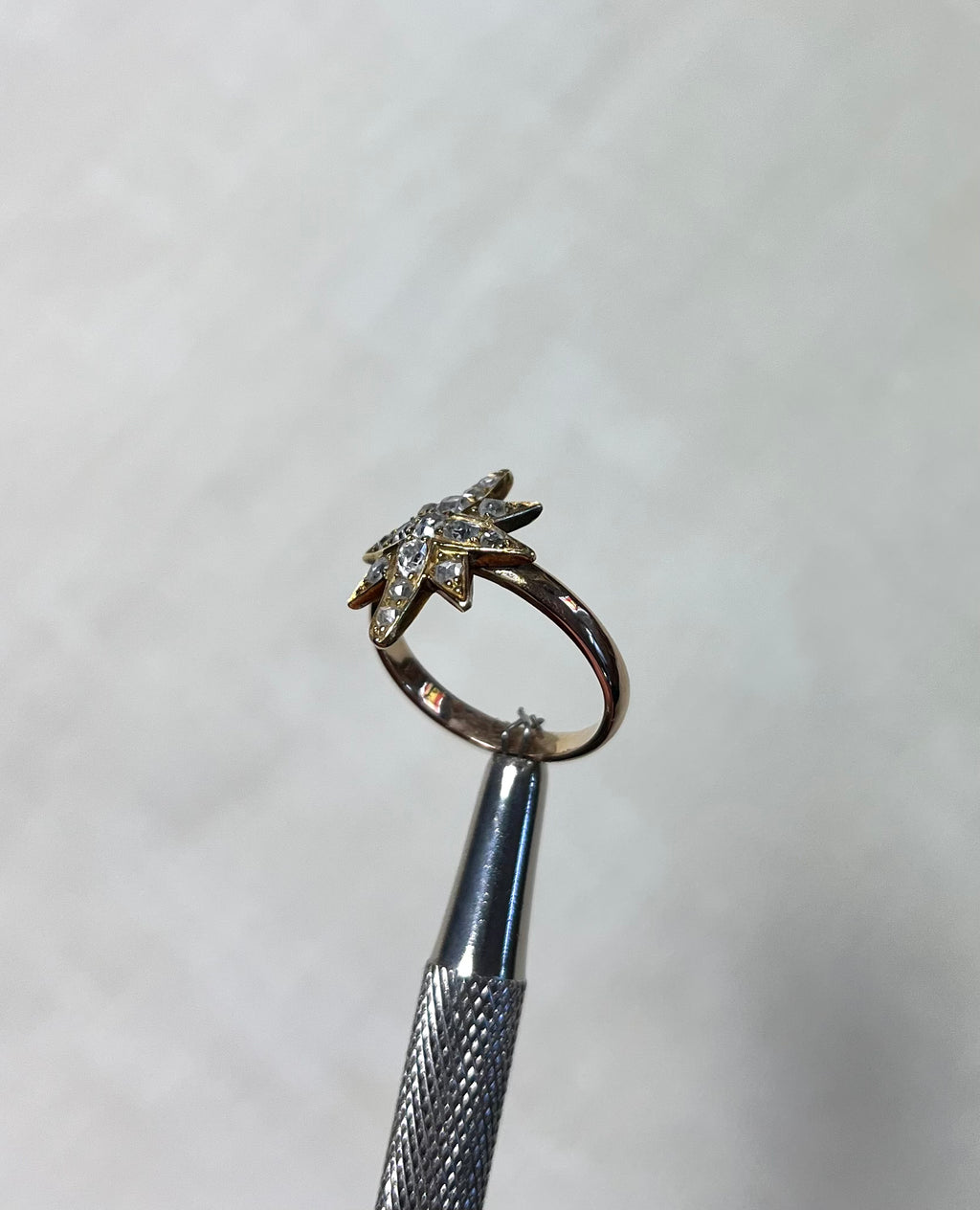 a gold star ring set with diamonds, held by silver tool above white background