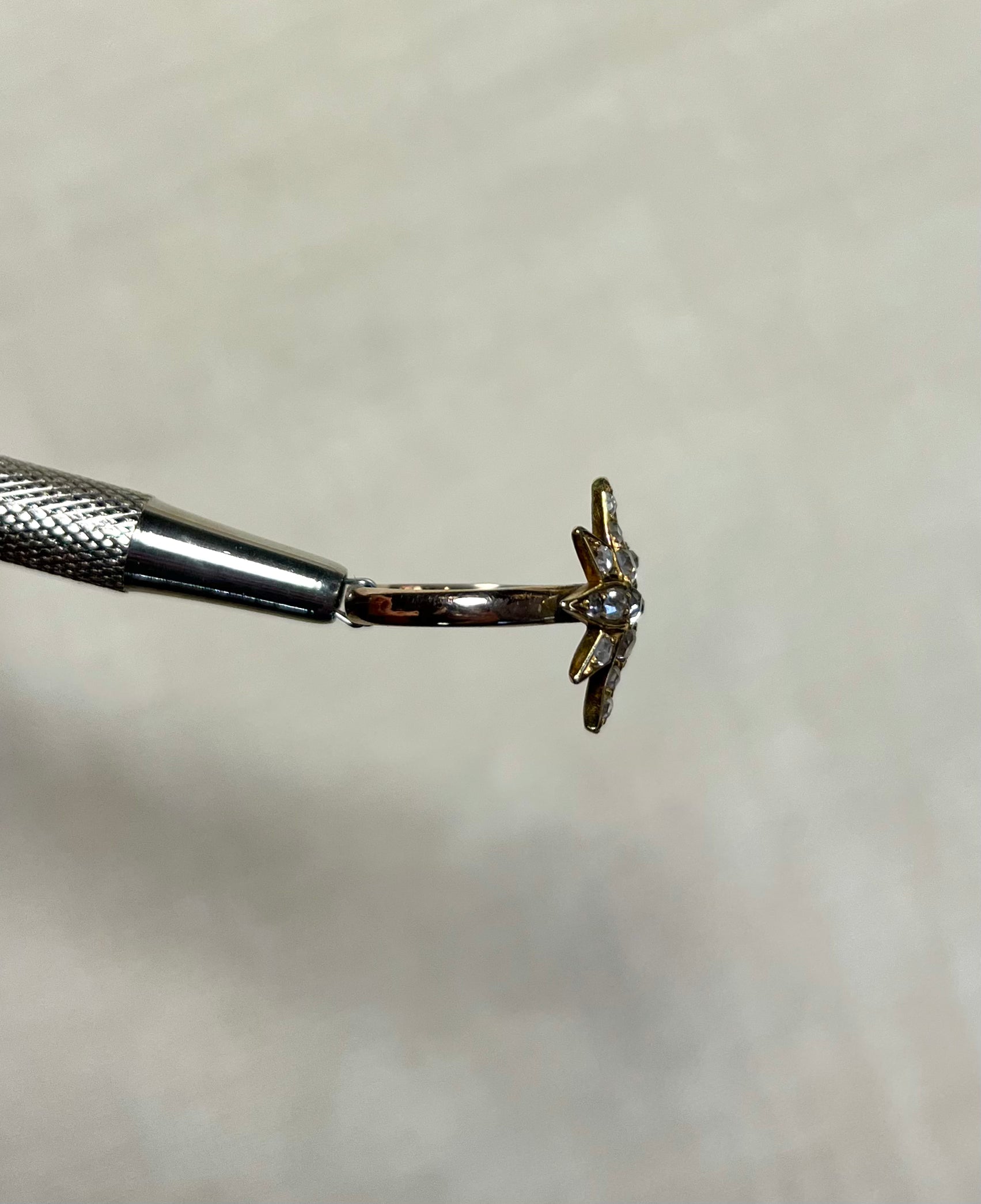 side view of gold star ring held by silver tool against white background