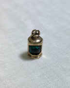 Gold pendant with a green centre in the shape of ship lantern on a white fabric background