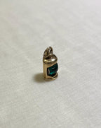 Gold pendant with a green centre in shape of ship lantern on a white fabric background 