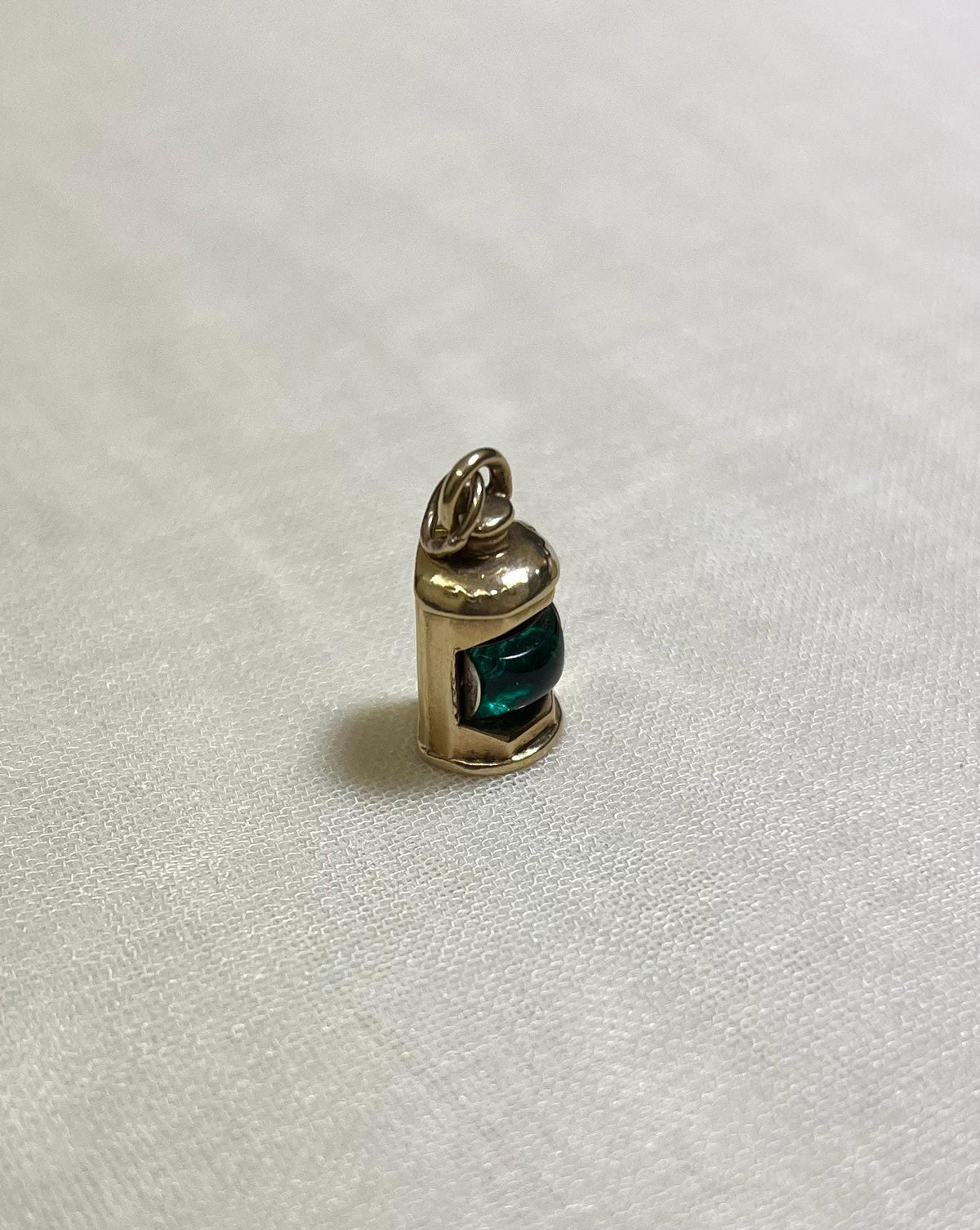 Gold pendant with a green centre in shape of ship lantern on a white fabric background 