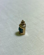Gold pendant with a green centre in shape of ship lantern on a white fabric background