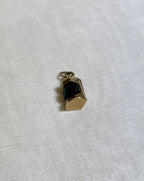 gold pendant in shape of ship lantern with green centre, resting on white fabric background 