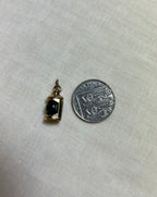 gold pendant with green centre next to ten pence coin for scale, on white fabric background