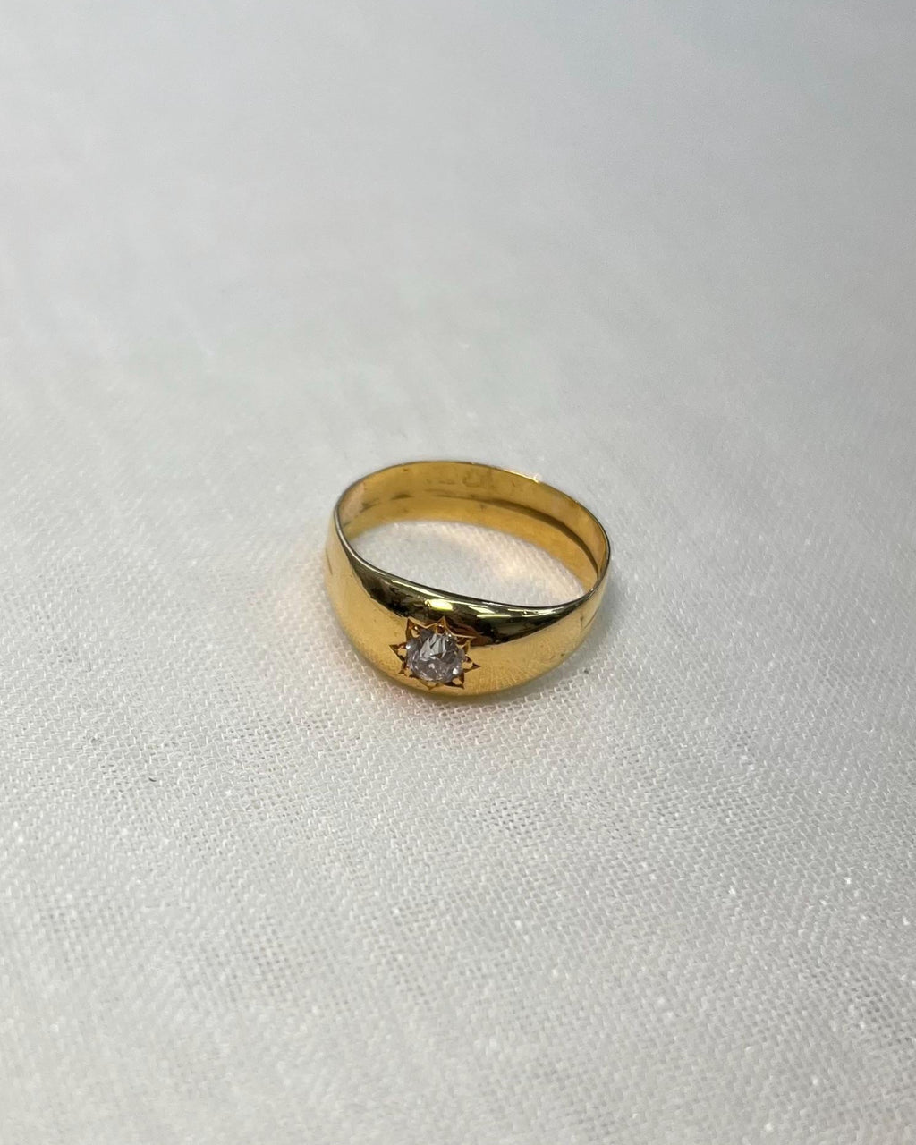 Gold ring with a diamond starburts design on a white fabric background