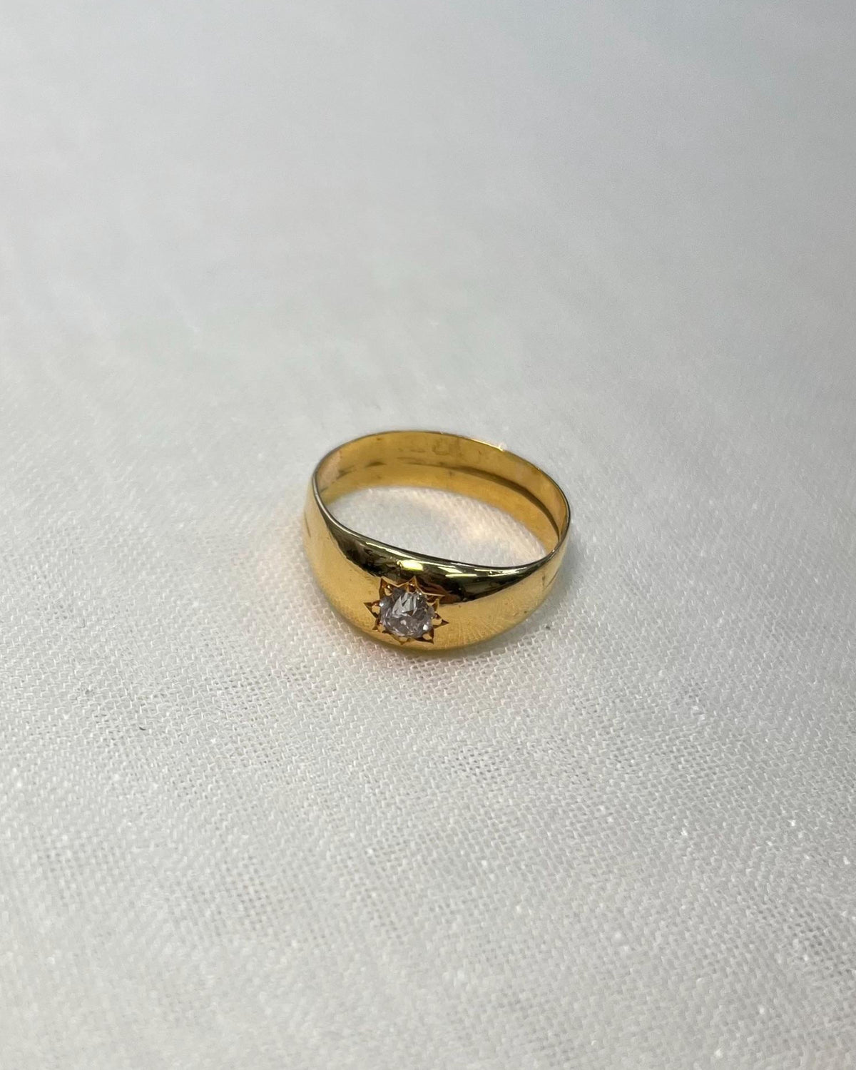 Gold ring with a diamond starburts design on a white fabric background