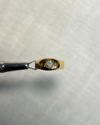 gold diamond starburst ring held by metal tool, with white background
