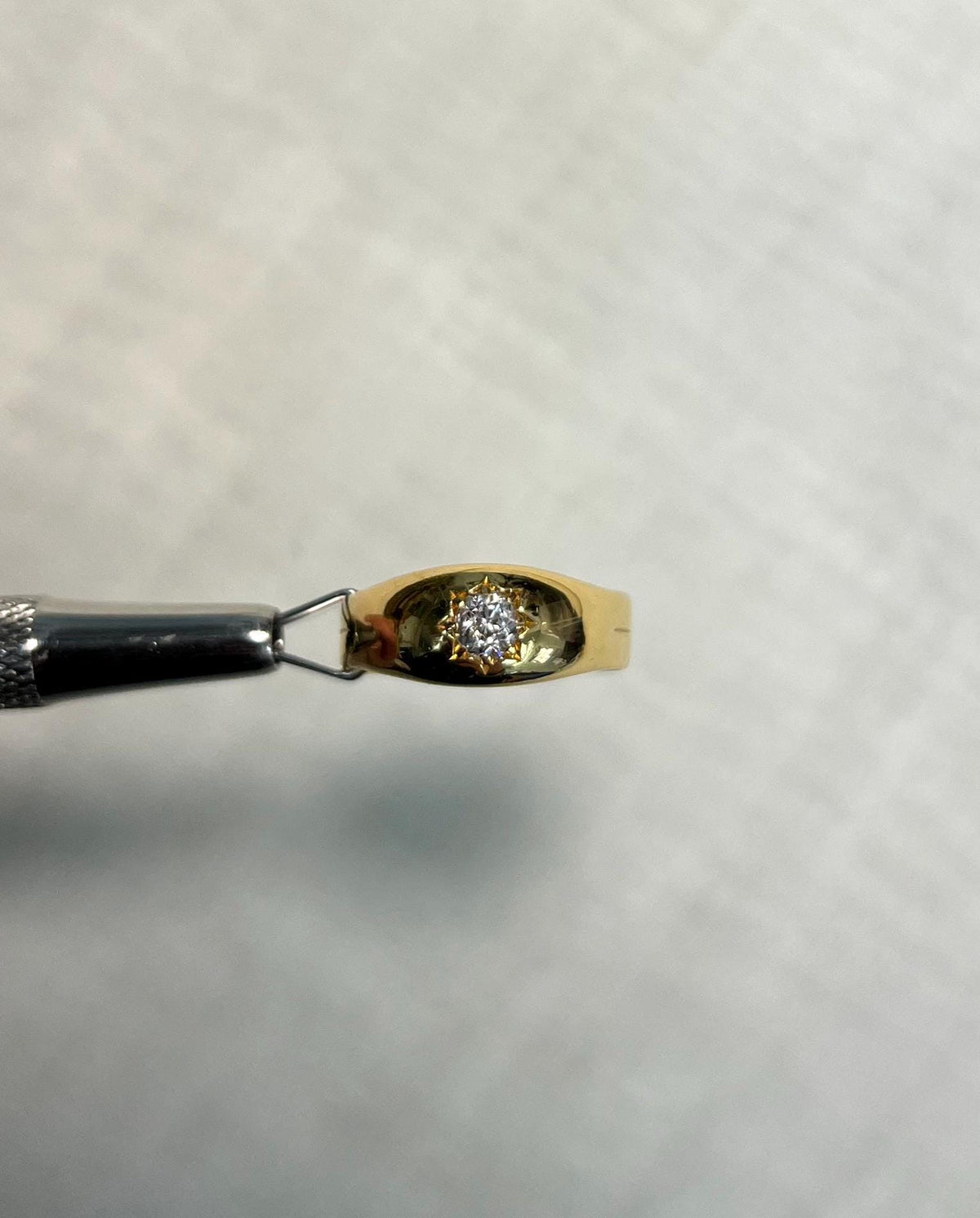 gold diamond starburst ring held by metal tool, with white background