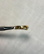 side view of gold ring with diamond, held by metal tool above white background 