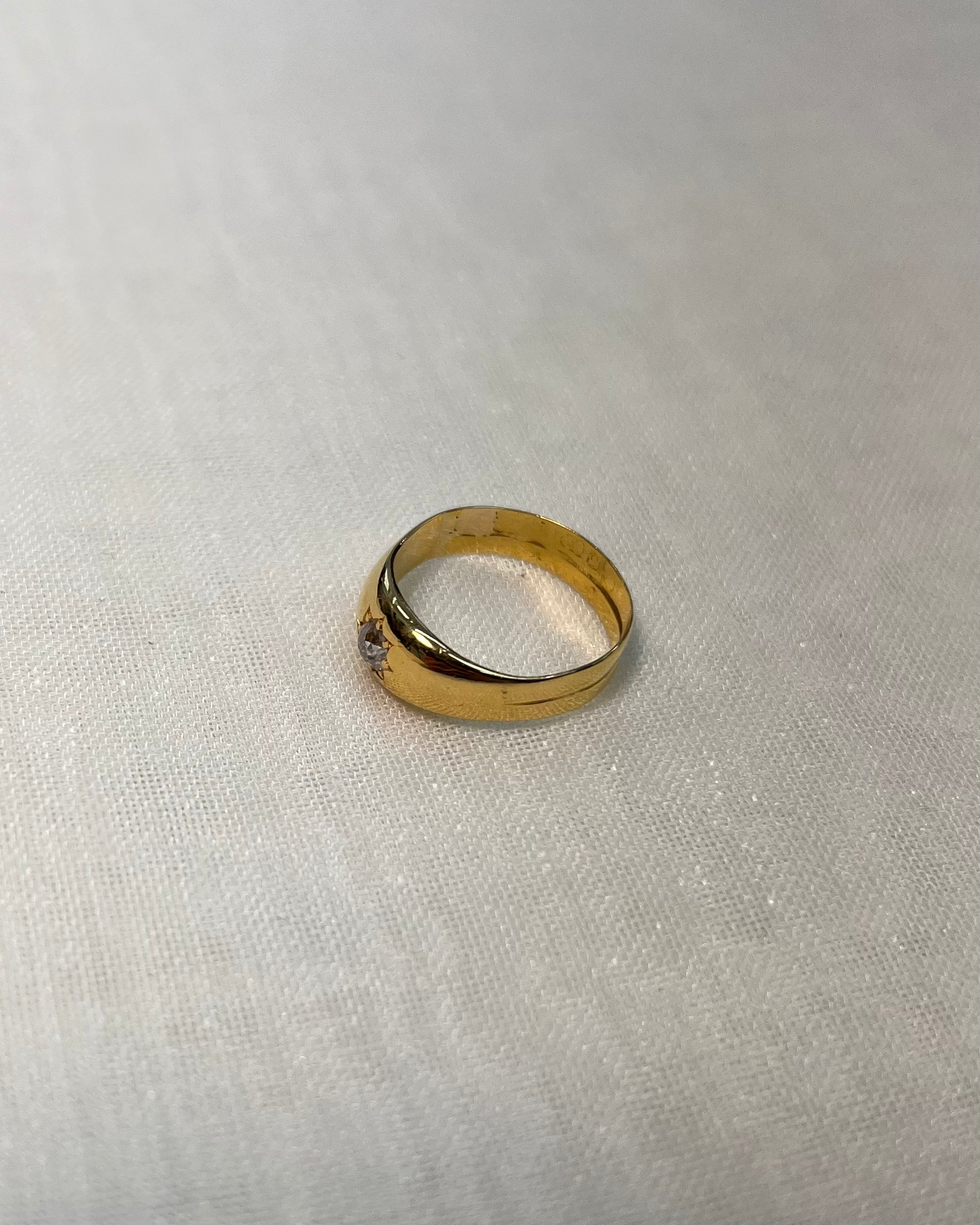 side view of a yellow gold ring with a diamond, photographed on a textured off-white fabric background.