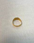 back view of gold ring set with diamond, resting on white fabric background 