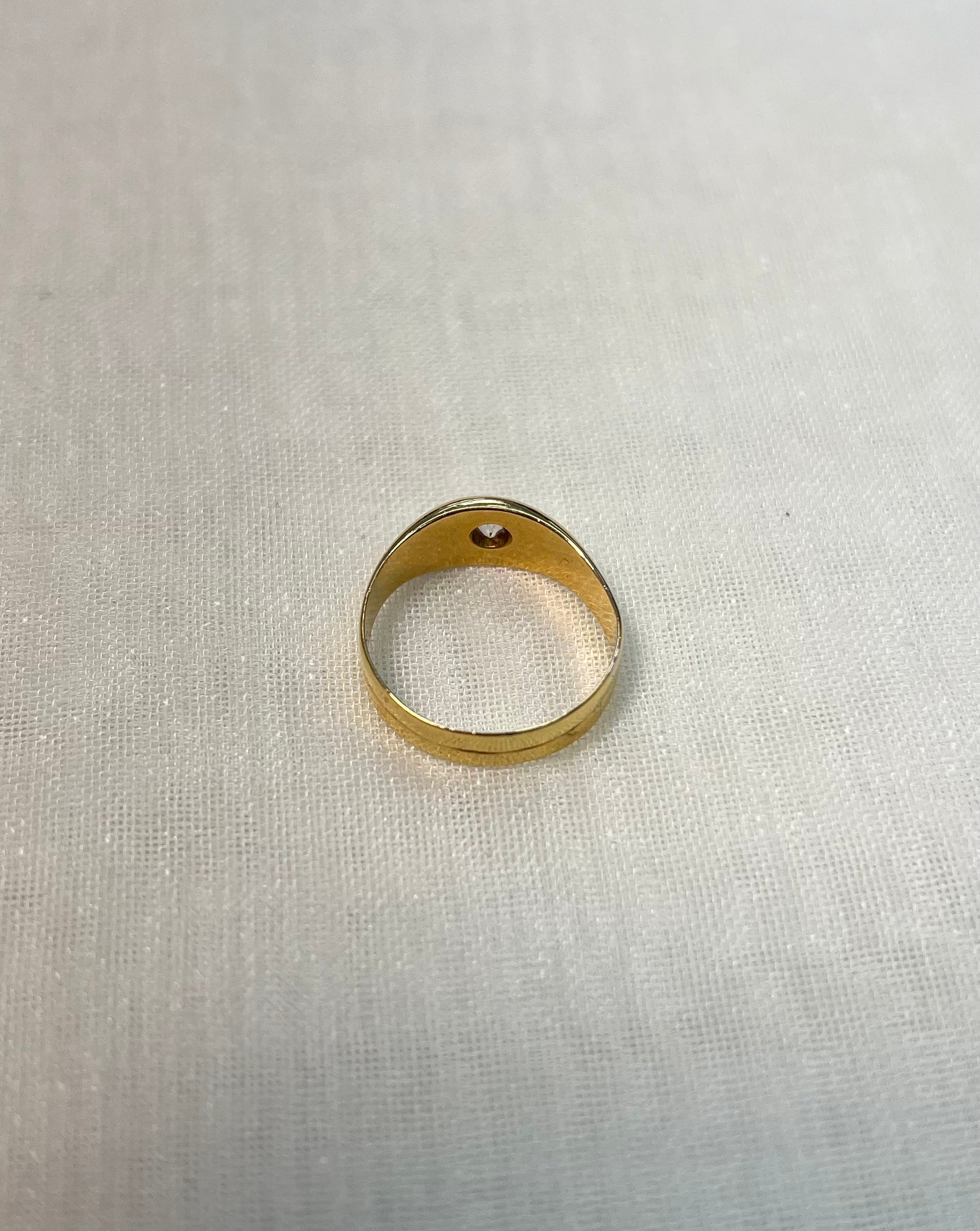 back view of gold ring set with diamond, resting on white fabric background 