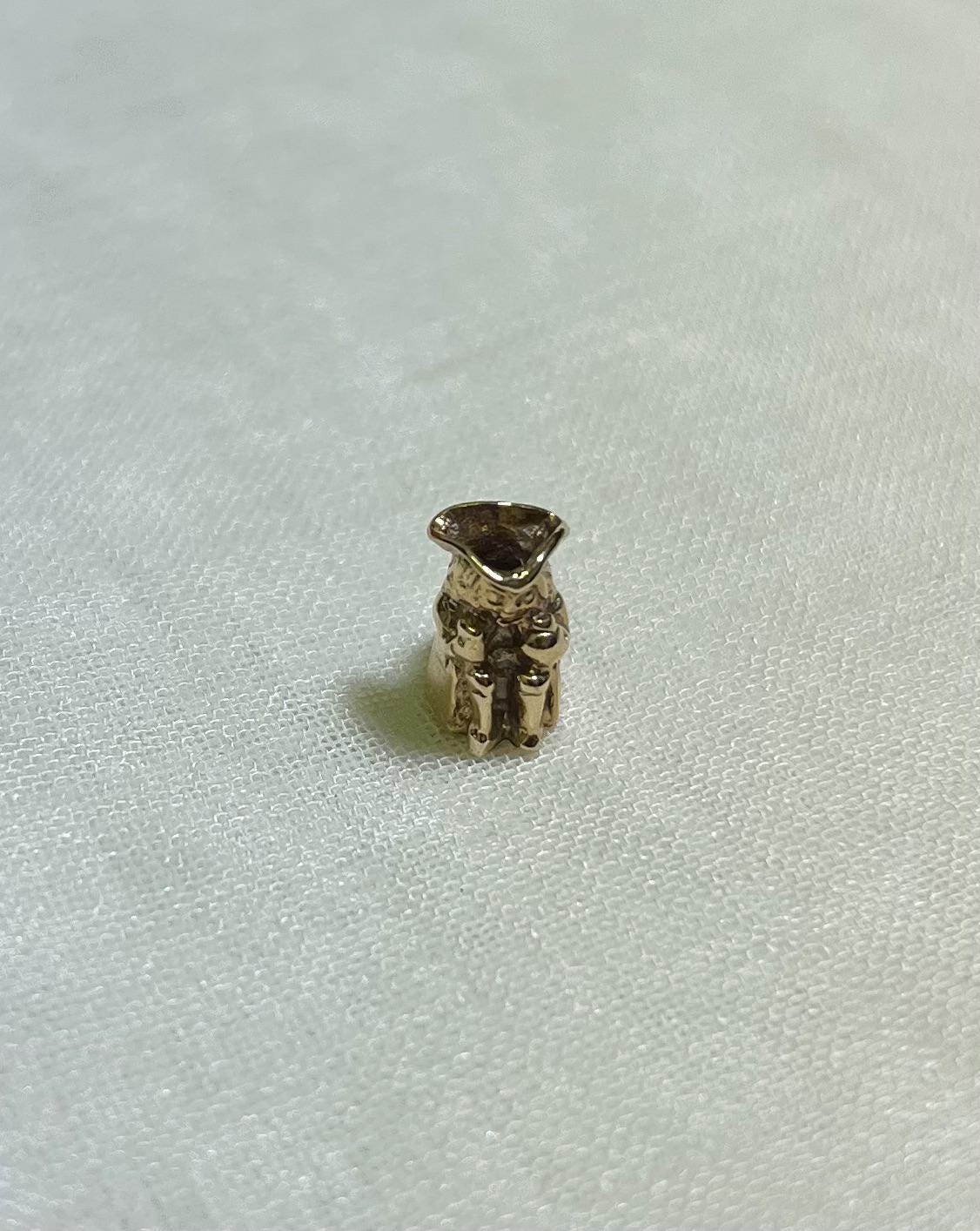 small gold toby jug charm on cream fabric background 