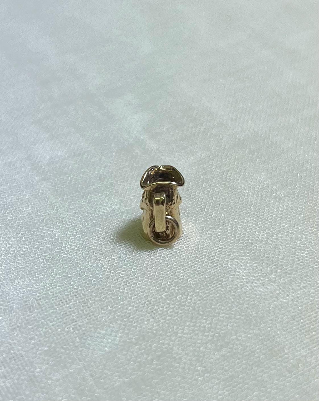 back view of small gold toby jug charm on cream fabric background