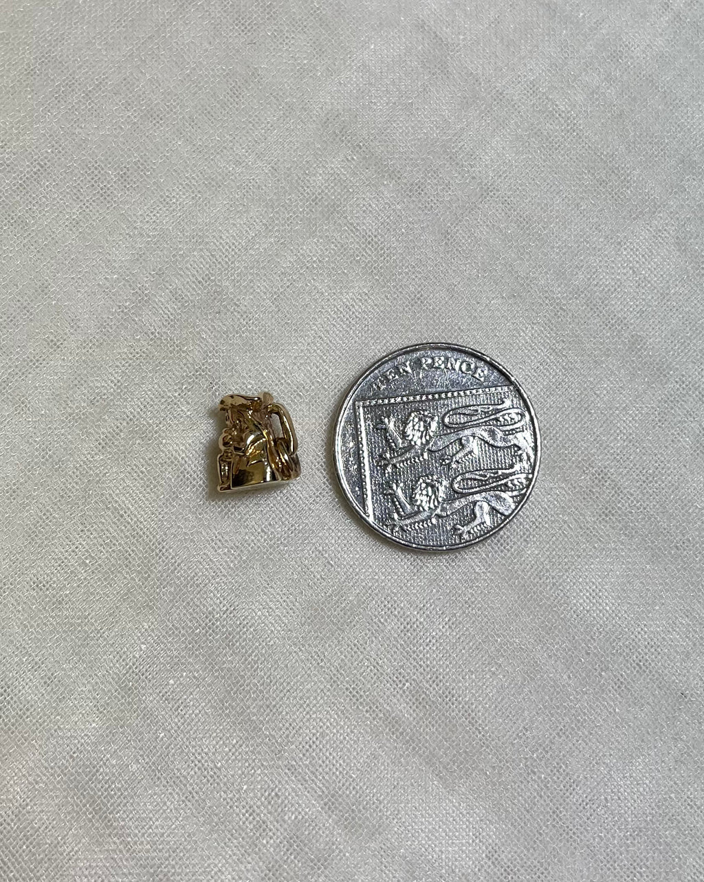 small gold toby jug charm next to ten pence coin on cream fabric background 