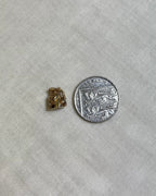 small gold toby jug charm next to ten pence coin on cream fabric background 