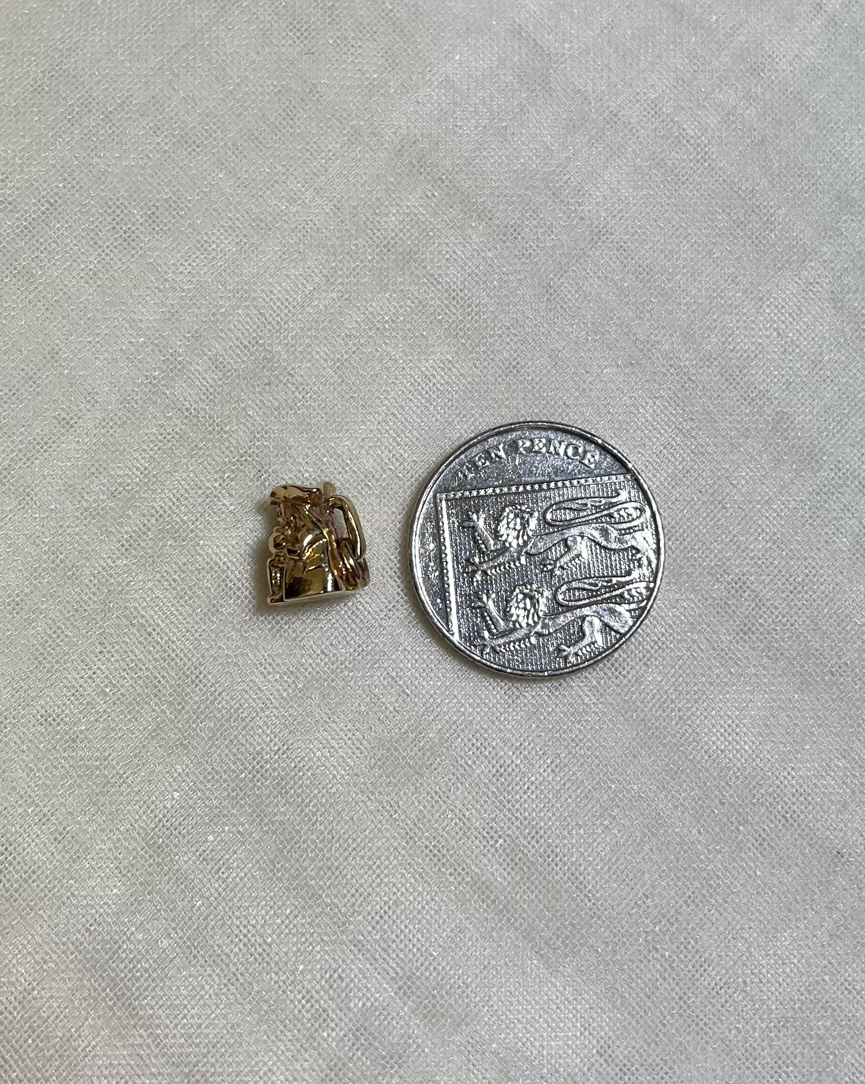 small gold toby jug charm next to ten pence coin on cream fabric background 