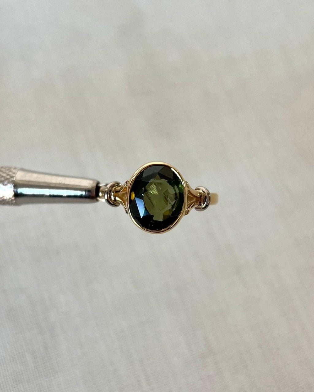 Gold ring with a oval green gemstone on a white background