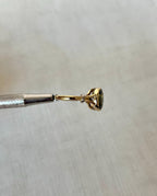 side view of gold ring with green gemstone held by silver tool above white background 