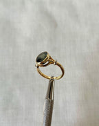 gold ring with green gemstone held by silver tool above white background 