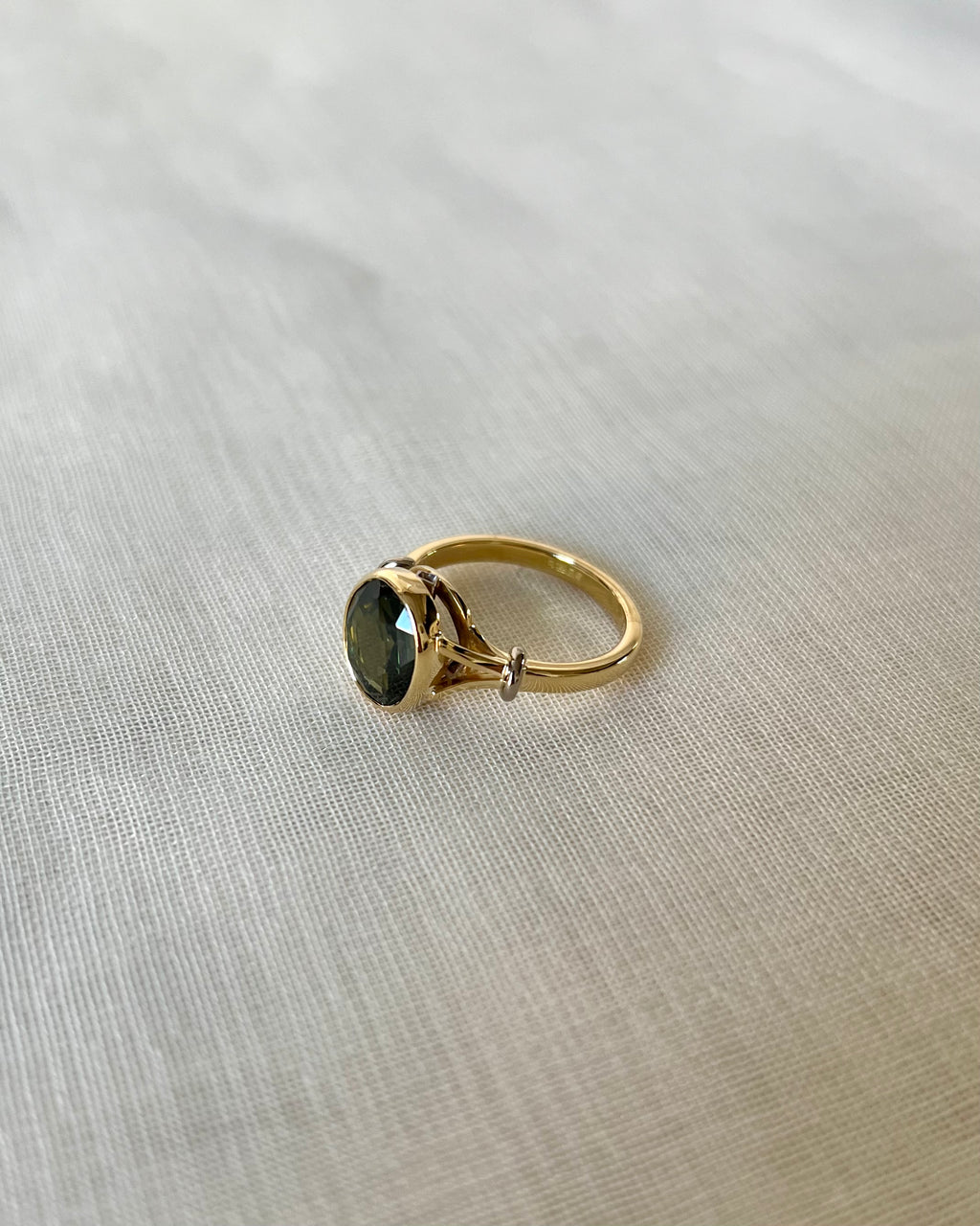 A gold ring with an oval dark green gemstone, resting on a textured beige fabric background.