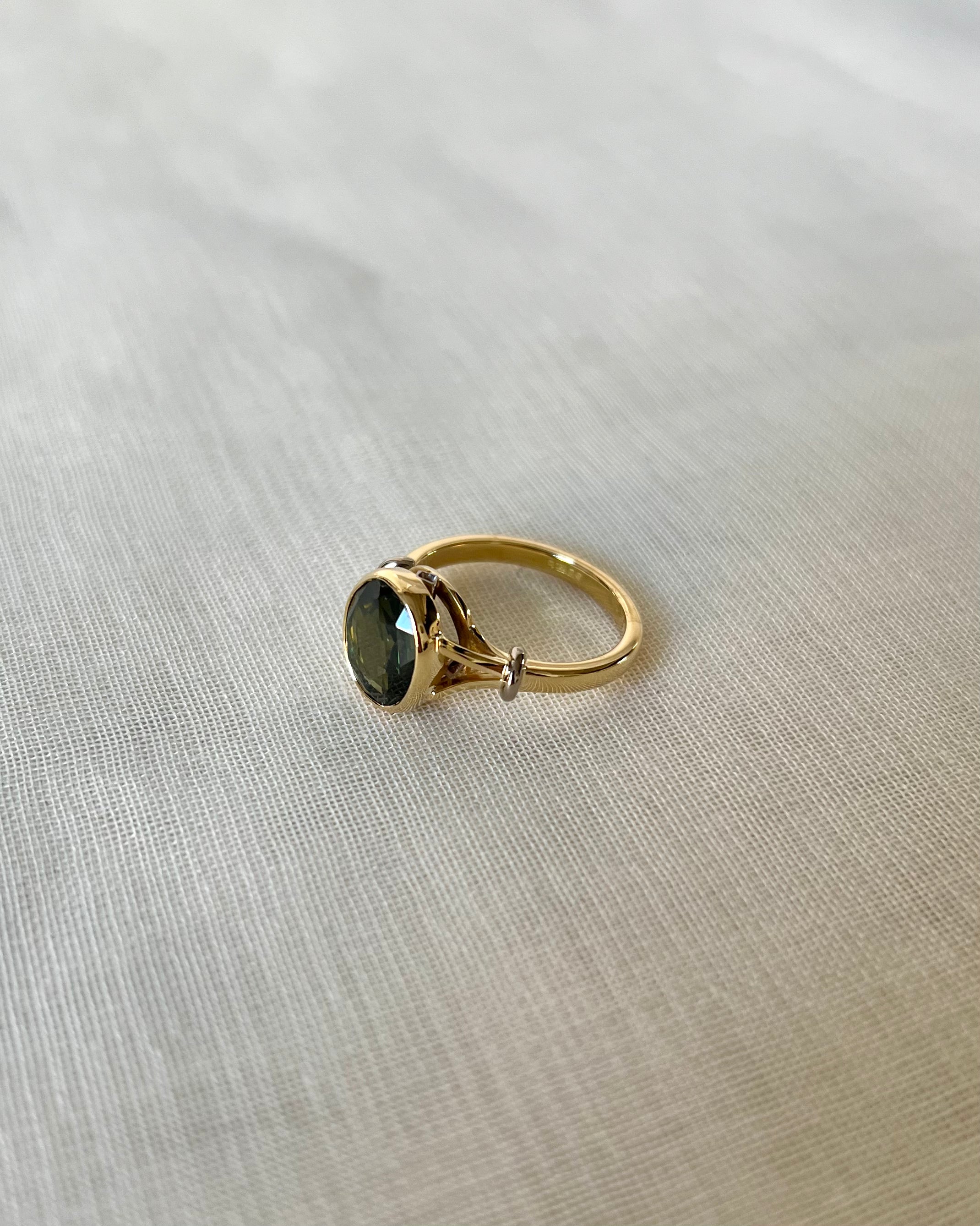 A gold ring with an oval dark green gemstone, resting on a textured beige fabric background.