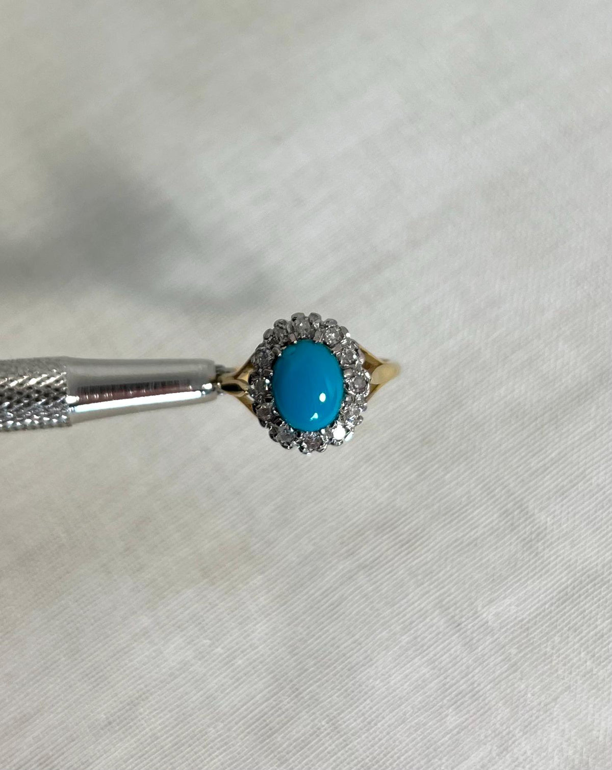 gold Ring with turquoise stone and diamond accents on a white fabric background