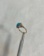 Gold ring with a turquoise gemstone and diamond stones on a textured cream background
