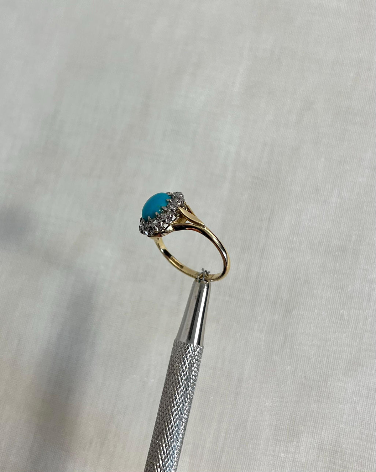 Gold ring with a turquoise gemstone and diamond stones on a textured cream background
