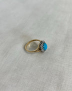 Gold ring with a turquoise gemstone and diamonds on a light fabric background
