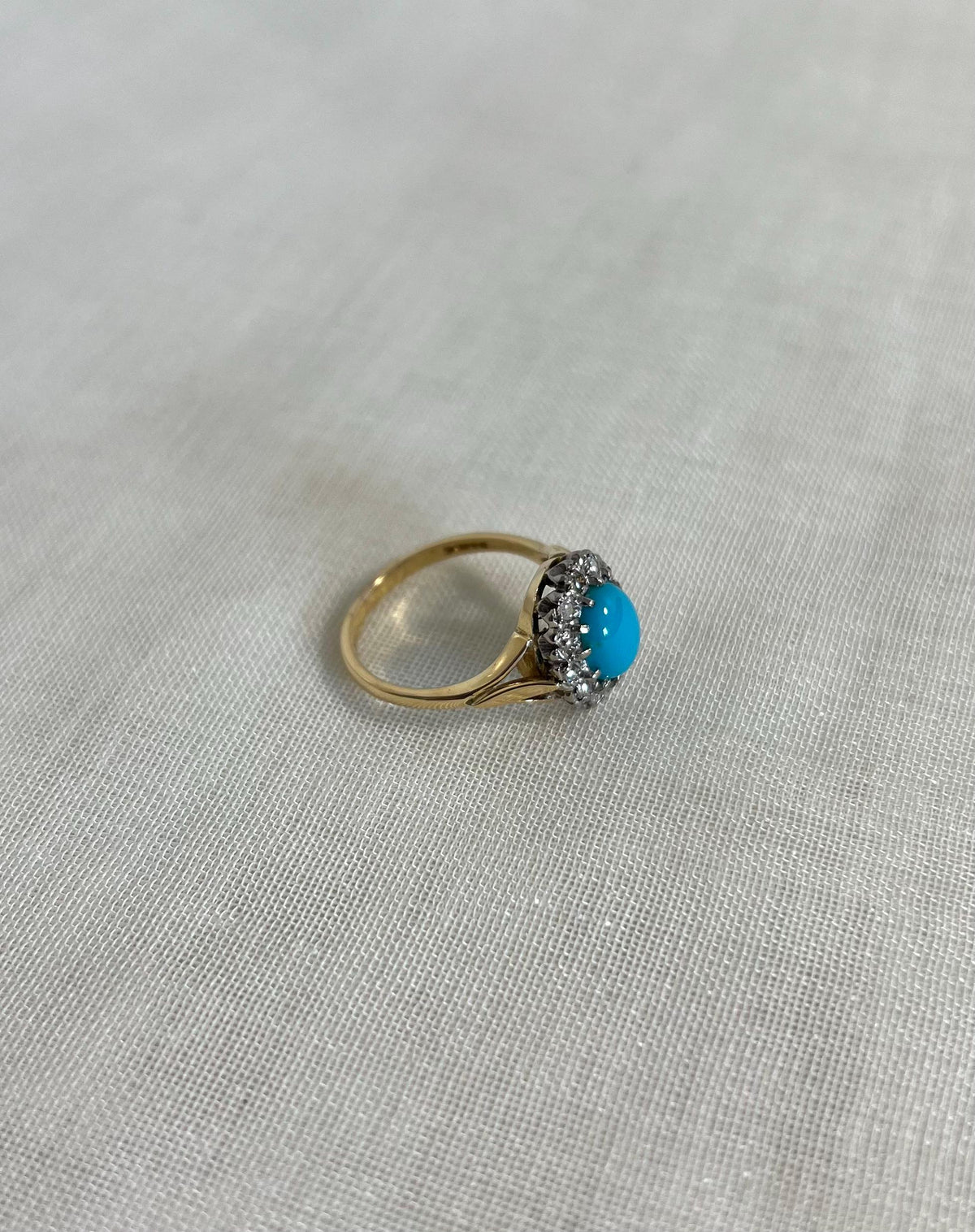 Gold ring with a turquoise gemstone and diamonds on a light fabric background