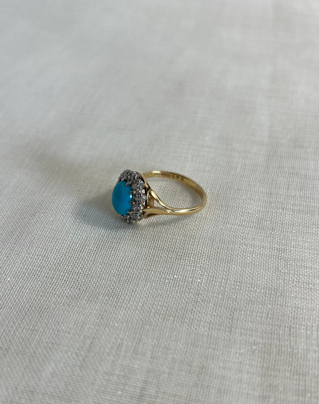 gold ring with turquoise and diamonds on light beige fabric background