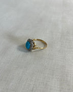 gold ring with turquoise and diamonds on light beige fabric background