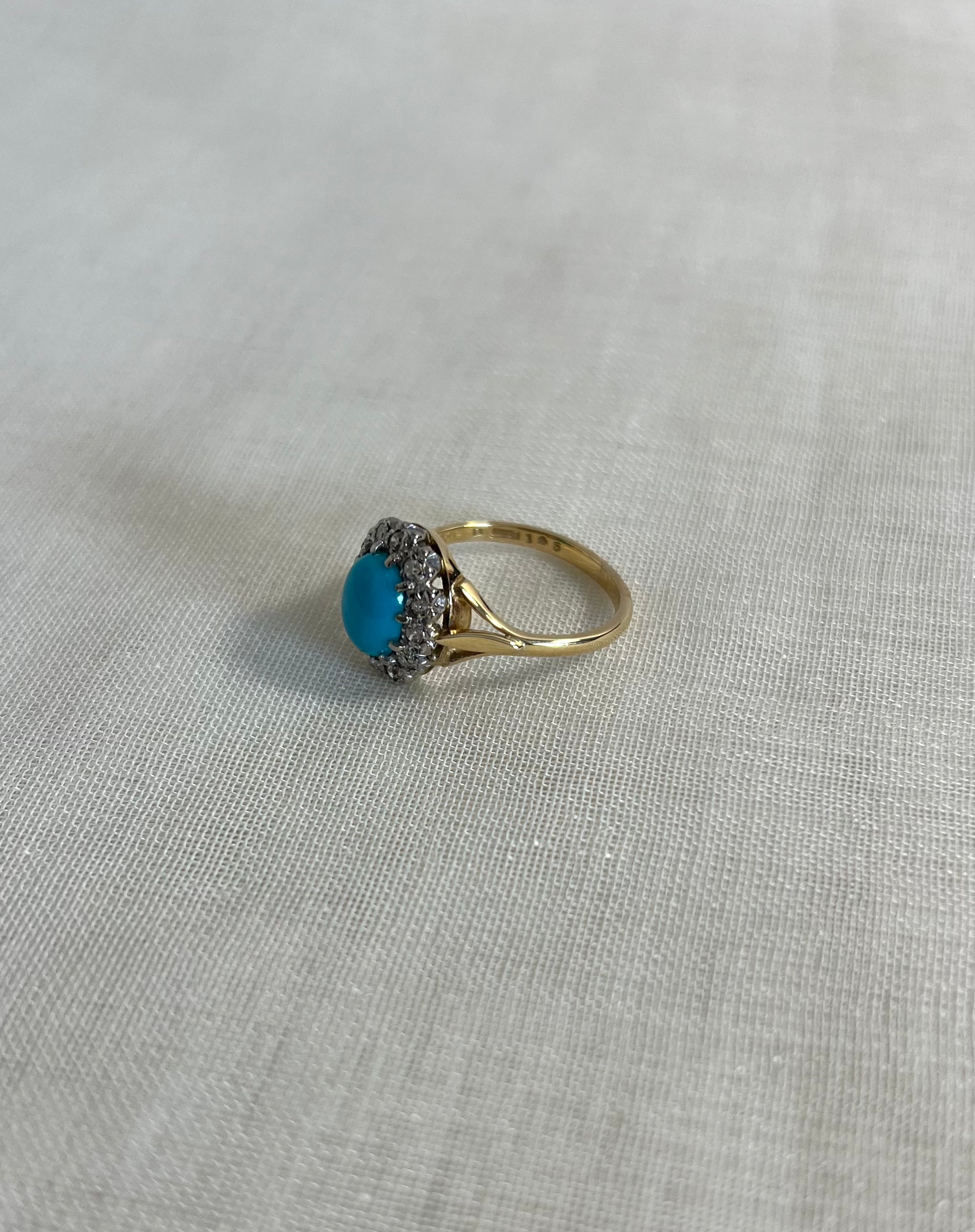 gold ring with turquoise and diamonds on light beige fabric background